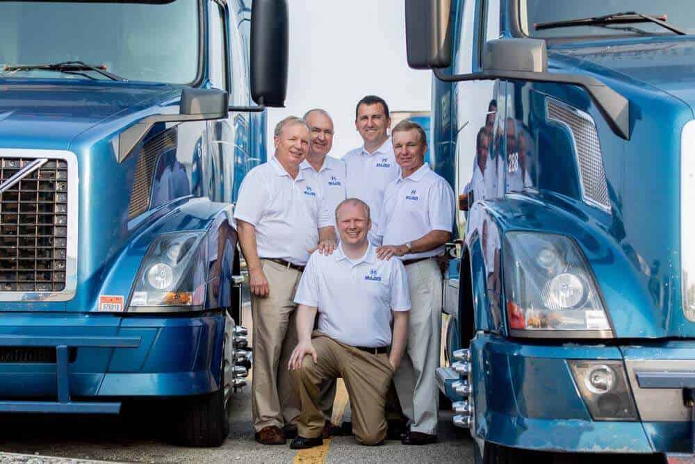 men posing next to two blue semi-trucks